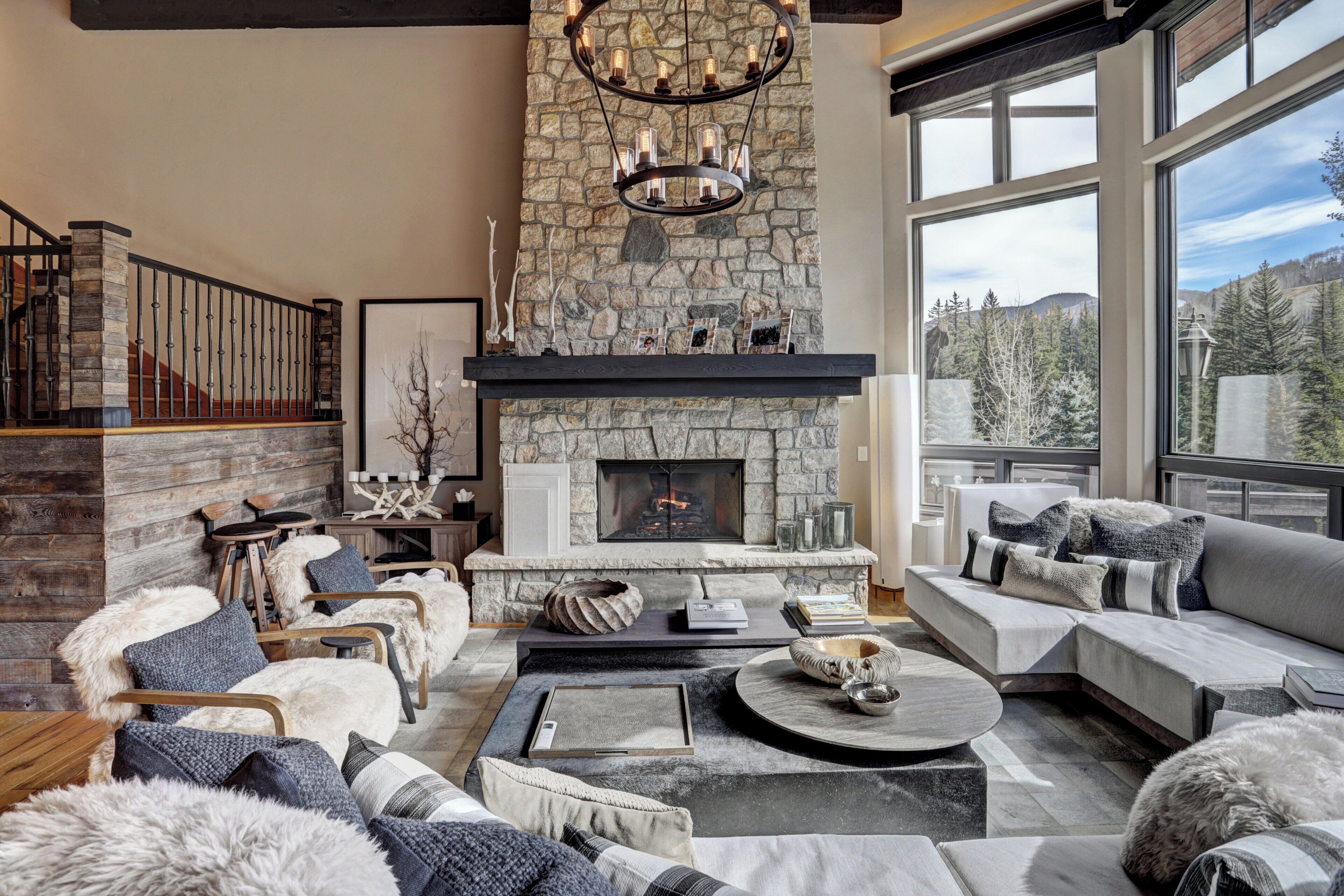 A cozy living room with a stone fireplace, comfortable seating, and a large window offering a mountain view.