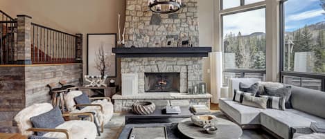 A cozy living room with a stone fireplace, comfortable seating, and a large window offering a mountain view.