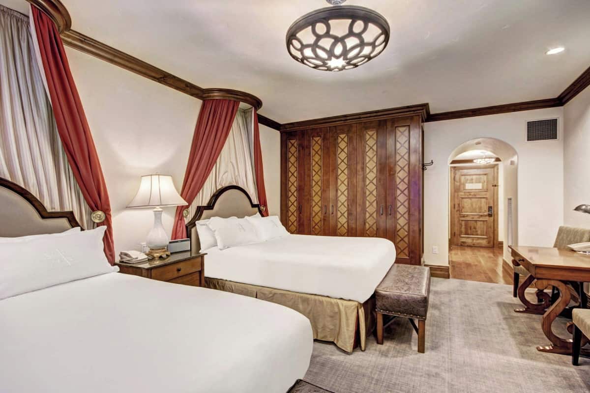 A hotel room with two beds, a desk, a chair, a lamp, and a wardrobe.