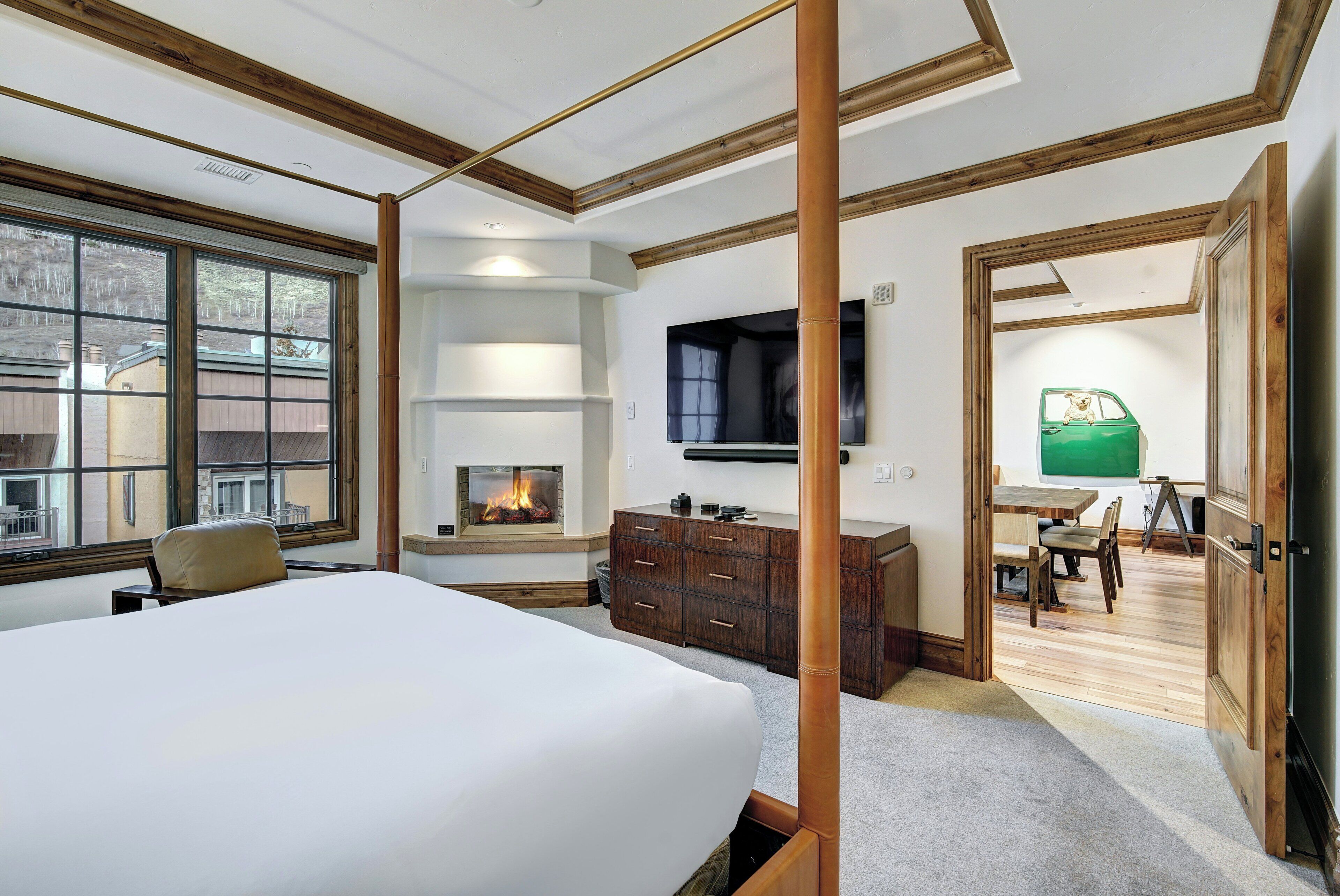A bedroom with a large bed, a TV mounted on the wall, a wooden dresser, and a fireplace.