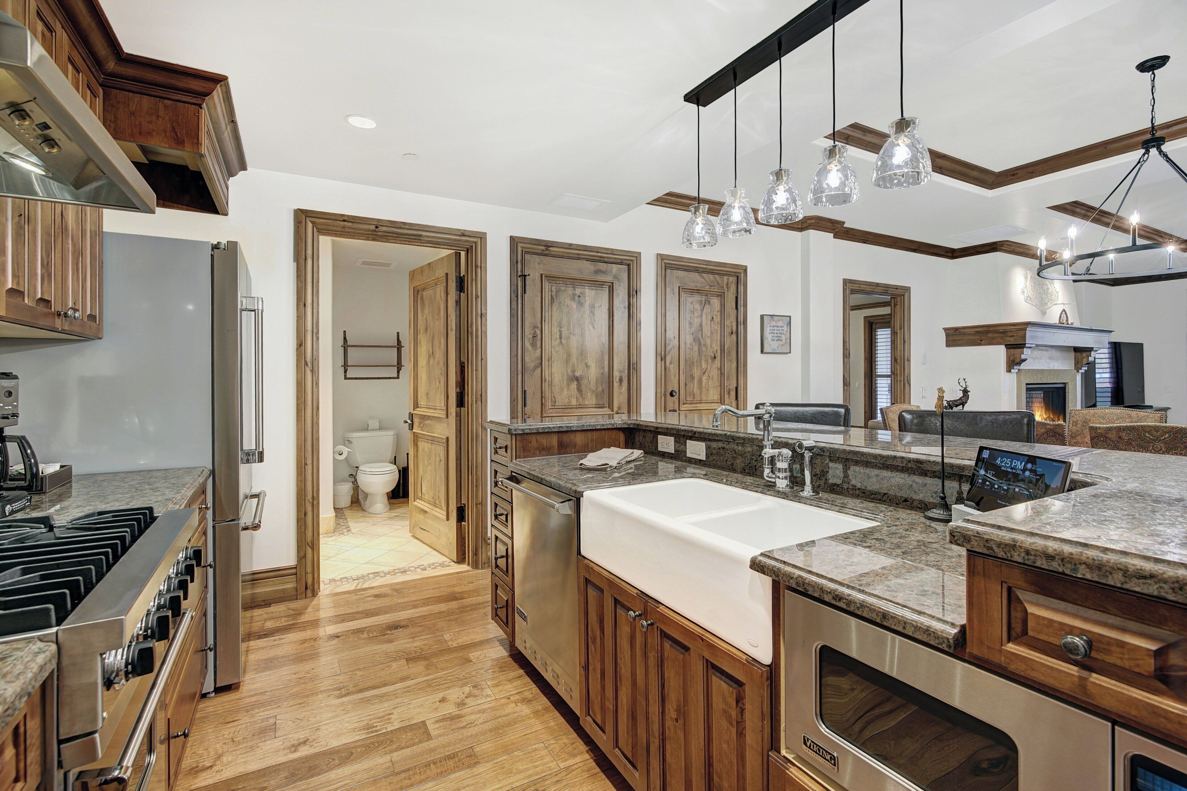 A modern kitchen with wooden cabinets, a stainless steel range, a large sink, and pendant lighting.