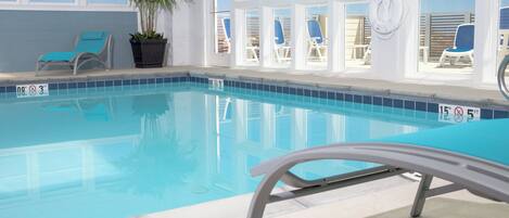 An indoor swimming pool with clear blue water, surrounded by windows and lounge chairs.