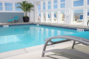 Une piscine intérieure à l’eau d’un bleu cristallin, entourée de baies vitrées et de chaises longues.
