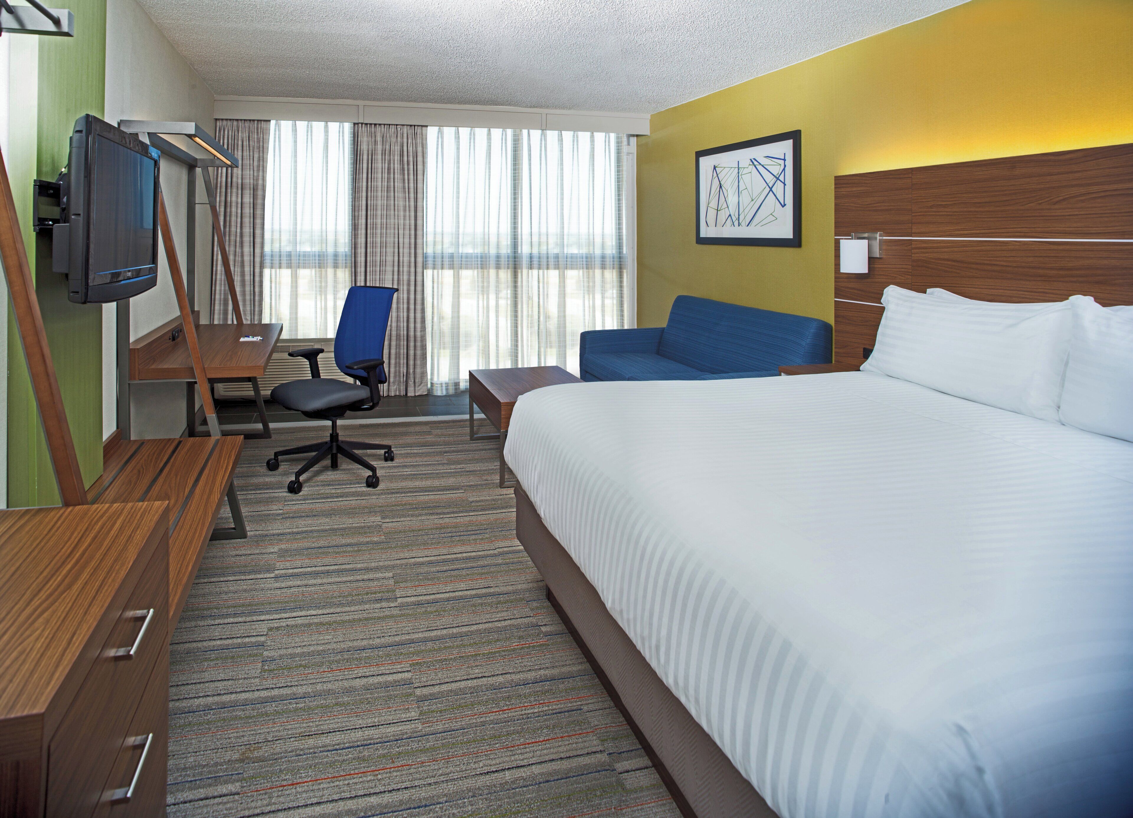A hotel room with a large bed, a desk with a chair, a television, and a window with curtains.