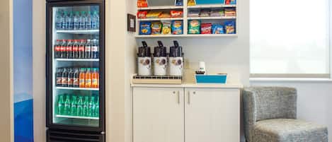 En automattank med olika drycker, en kaffemaskin, hyllor med snacks och en sittplats.