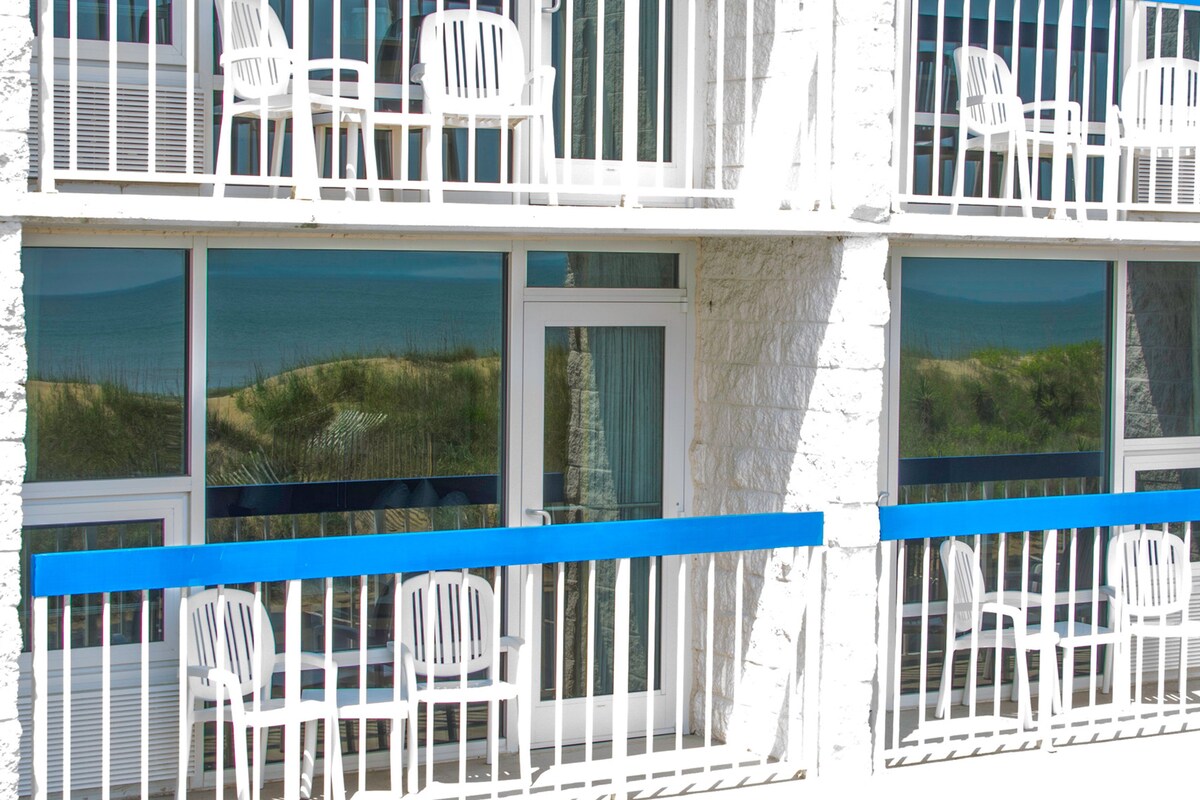 Een gebouw met meerdere balkons, elk voorzien van witte kunststof stoelen en een blauwe reling.