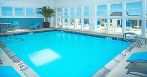 A swimming pool with clear blue water, surrounded by windows and chairs. - Holiday Inn Express Nags Head Oceanfront by IHG (Nags Head)