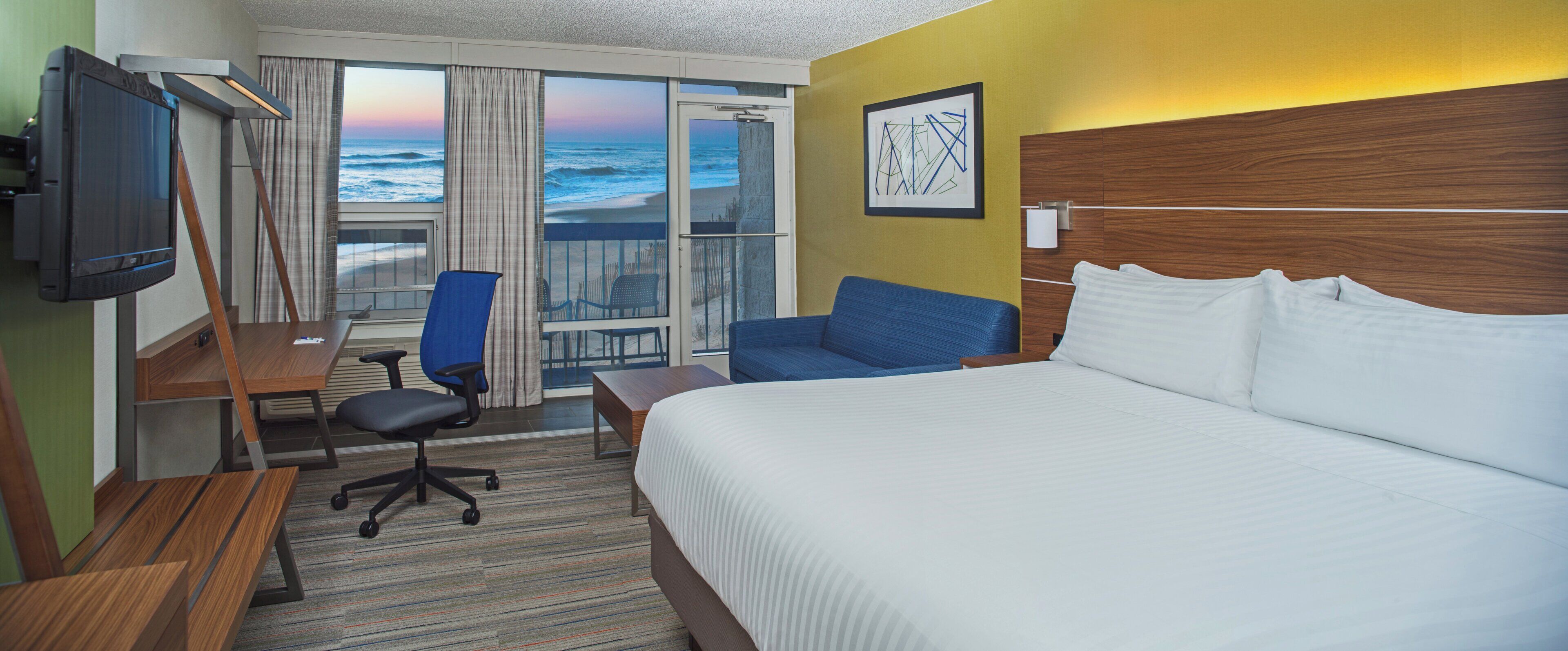 A hotel room with a bed, a desk, a chair, a TV, and a window with a view of the ocean.