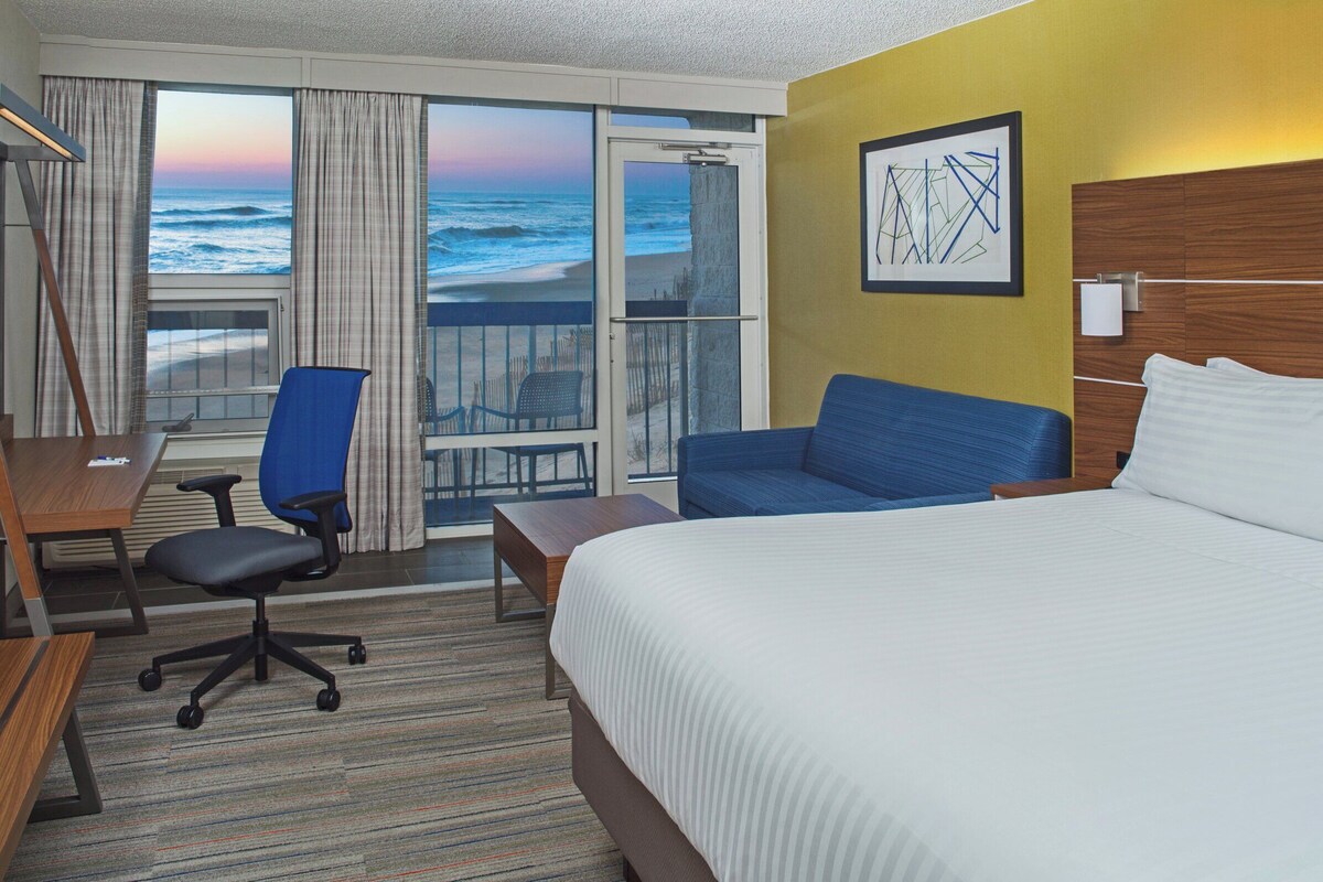 Een hotelkamer met een bed, een bureau, een stoel, een televisie en uitzicht op de oceaan.