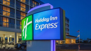 A Holiday Inn Express sign with a large 'H' logo, a building with multiple floors, and an American flag. - Holiday Inn Express Nags Head Oceanfront by IHG (Nags Head)