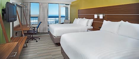 A hotel room with two beds, a desk, a chair, a TV, and a balcony with a view of the ocean.