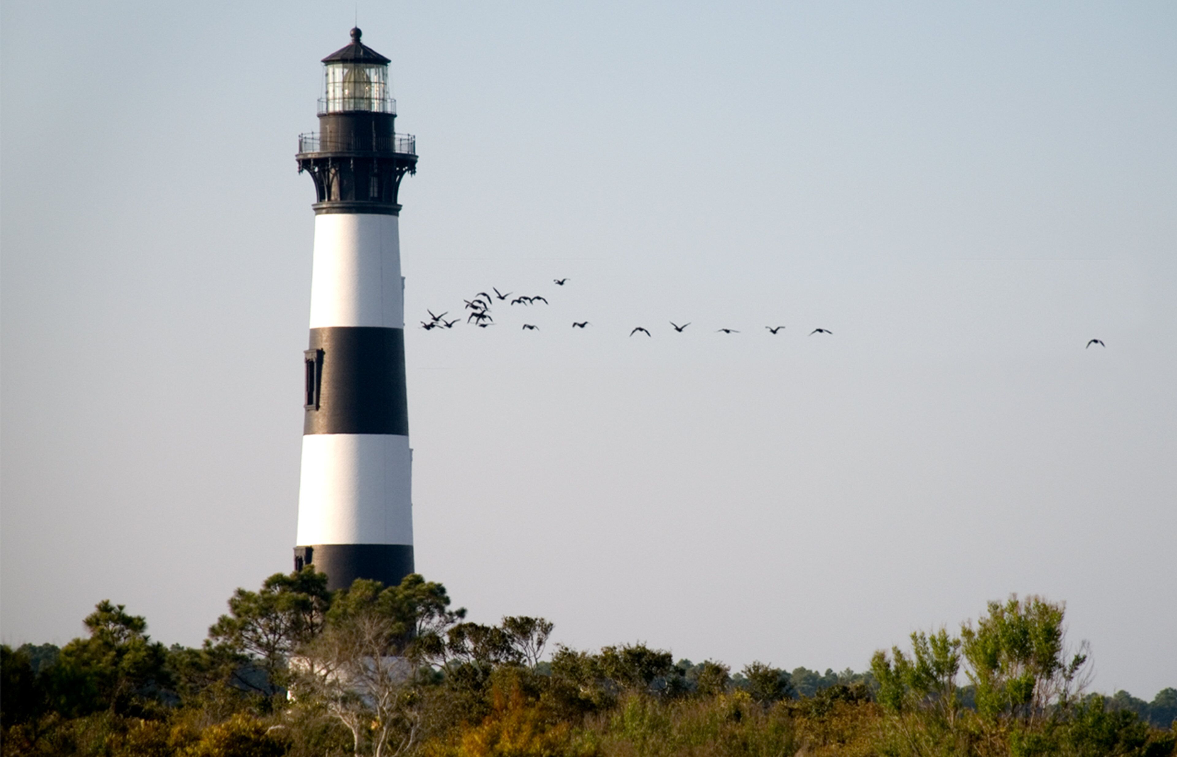 A lighthouse with a clear sky and birds flying in the distance.