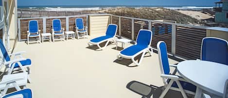 A beachside patio with lounge chairs and a table, overlooking the ocean.