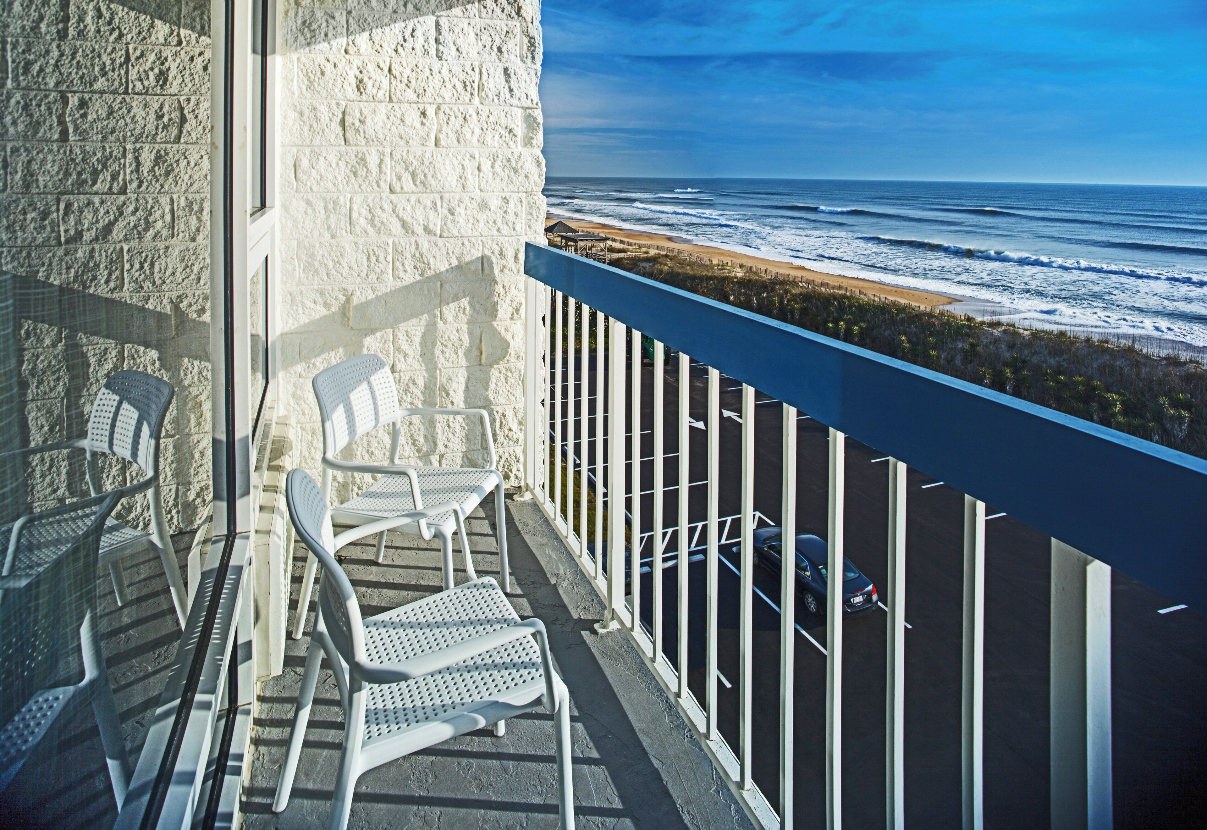 A balcony with white metal chairs and a view of the ocean.
