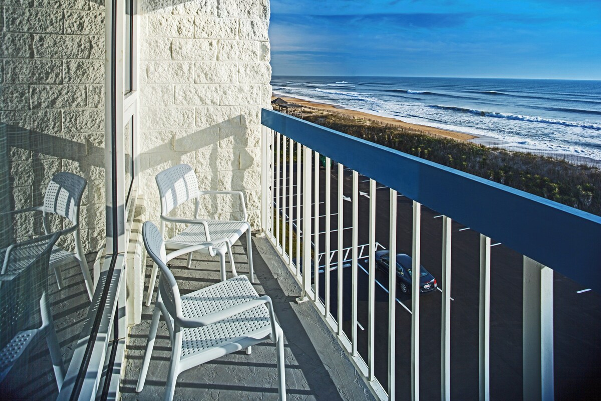 Een balkon met witte stoelen en uitzicht op de oceaan.