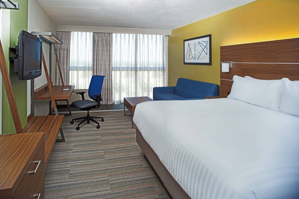 Une chambre d’hôtel avec un grand lit, un bureau avec une chaise, une télévision et une fenêtre avec des rideaux.