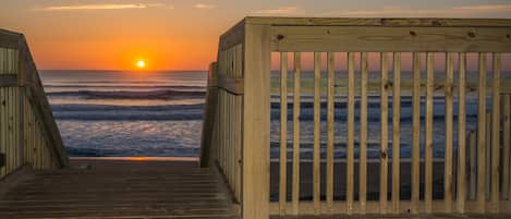 A wooden boardwalk leading to the ocean with a sunset in the background.
