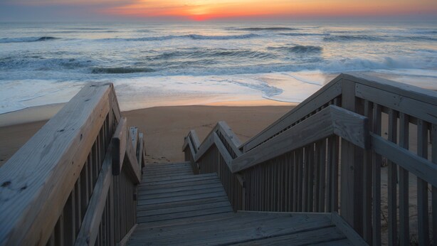 A wooden staircase leading to a beach with a sunset in the background. - Holiday Inn Express Nags Head Oceanfront by IHG (Nags Head)