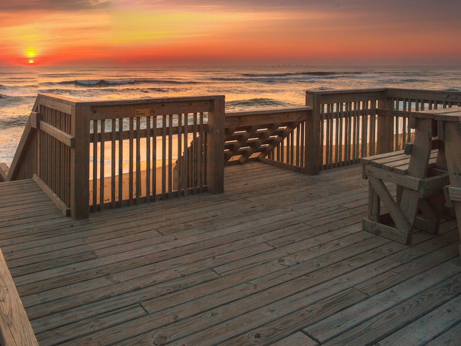 A wooden deck with benches overlooking the ocean at sunset.