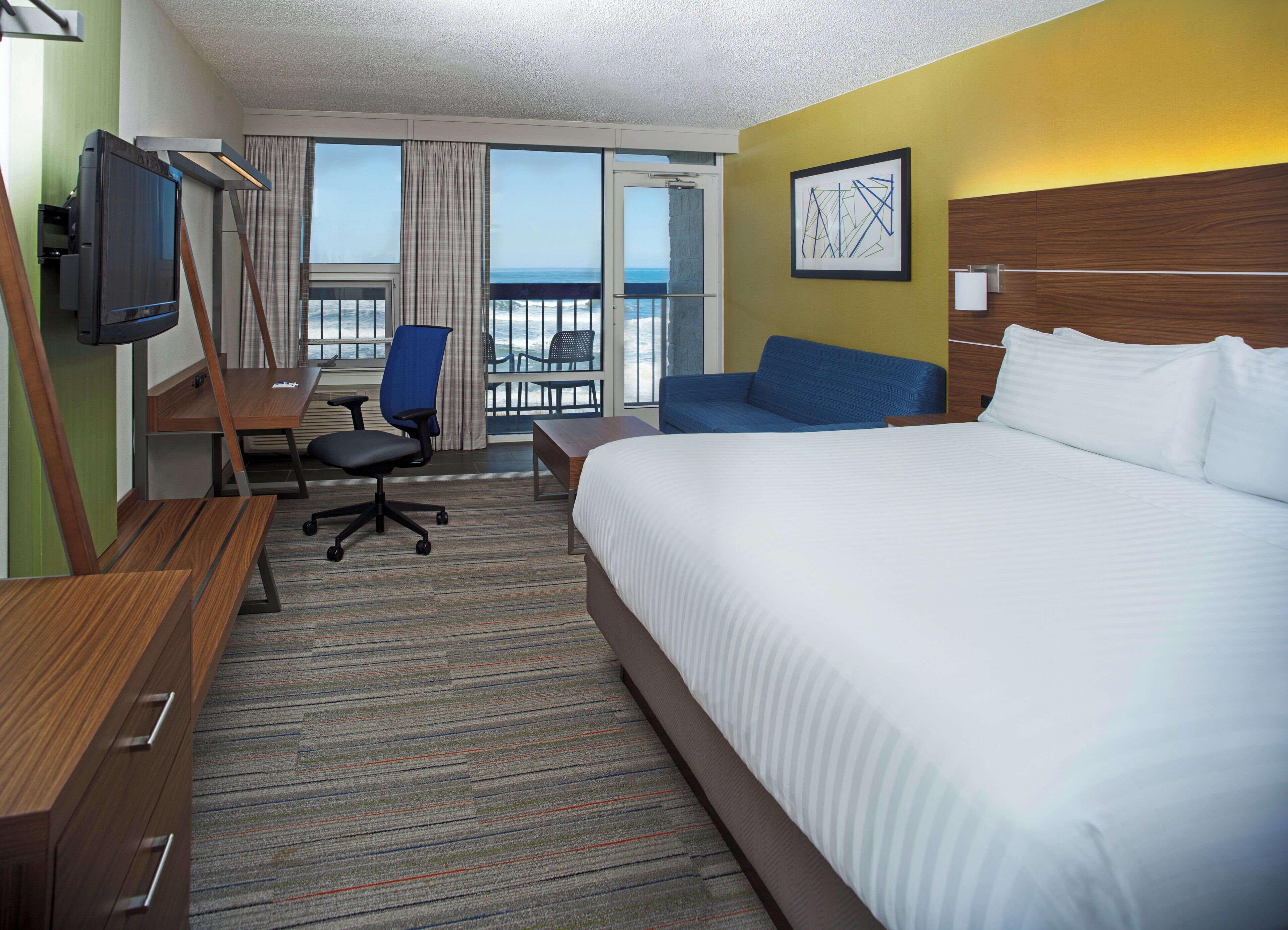 Une chambre d’hôtel avec un lit, un bureau, une chaise, une télévision et une vue sur l’océan.