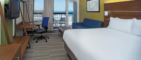 A hotel room with a bed, a desk, a chair, a television, and a view of the ocean.