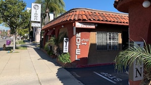 Un motel con techo de tejas rojas, un letrero que indica disponibilidad y un cartel que dice 'Oficina del Motel' señalando a la derecha.