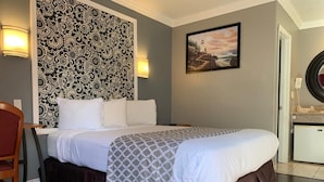 Una habitación de hotel con una cama grande, un cabecero estampado, un cuadro en la pared y un escritorio con una silla.
