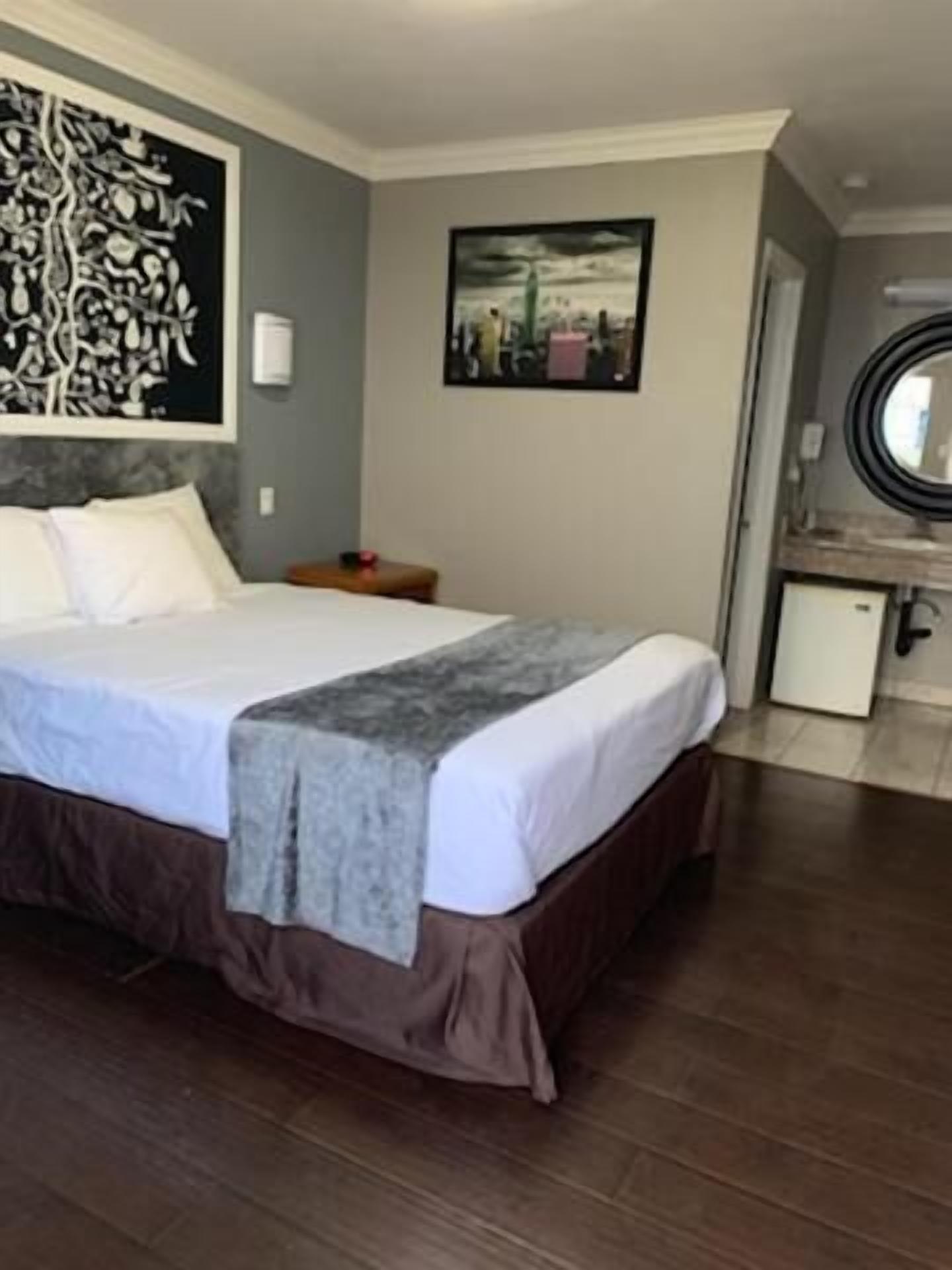Habitación de hotel con una cama grande, un escritorio pequeño, un espejo y un cuadro en la pared.