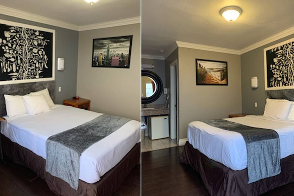 A hotel room with a large bed, a desk, and a chair. There is a painting on the wall and a small table with a lamp.