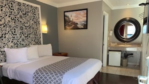 Una habitación de hotel con cama, pared con estampado, pintura de un faro, espejo redondo y una pequeña kitchenette.