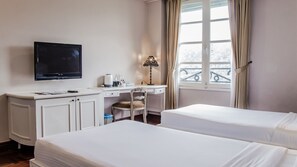 A hotel room with a bed, a desk with a computer, a TV, and a window with curtains.