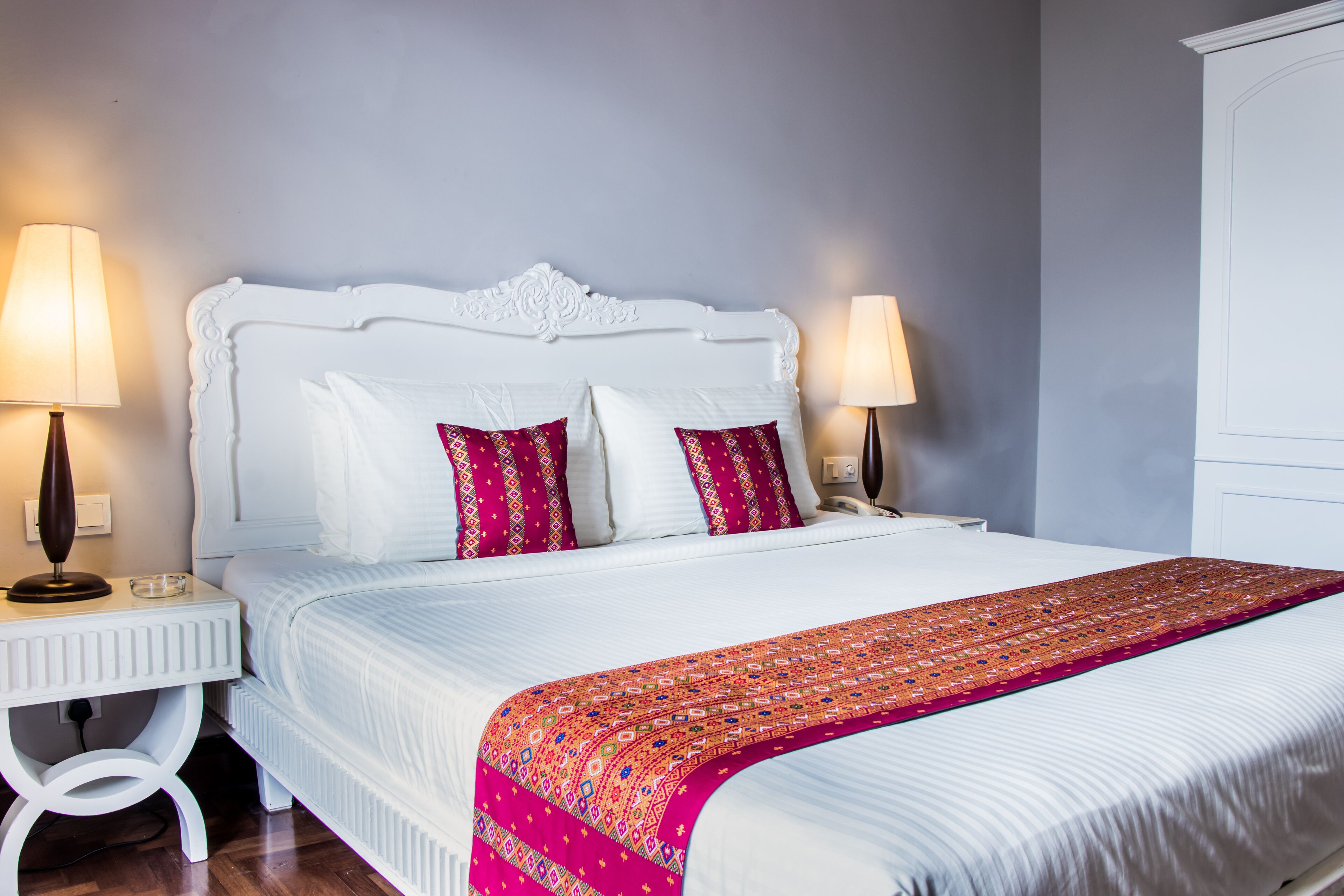 A neatly made bed with a white headboard, two bedside lamps, and a patterned throw blanket.