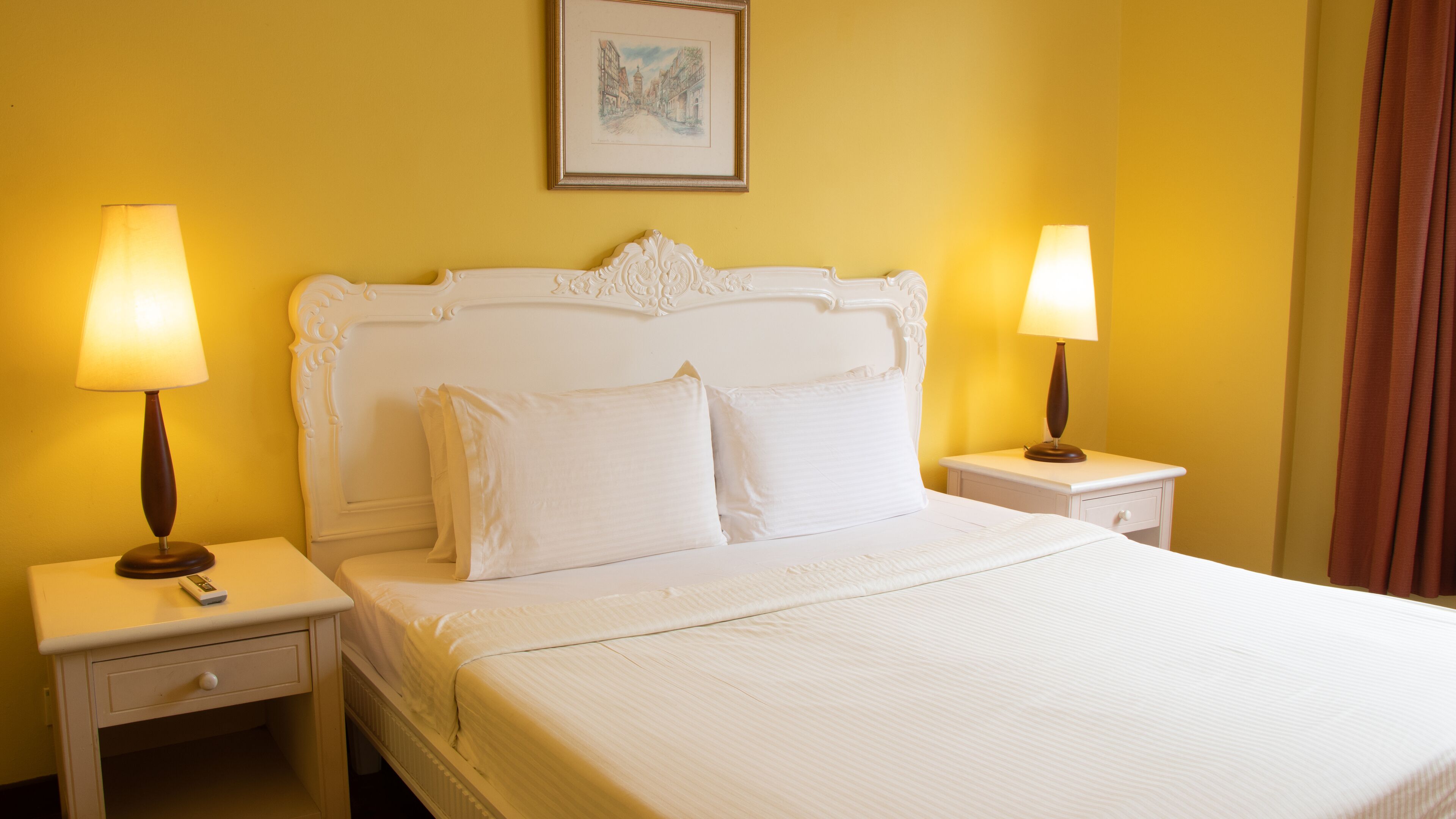 A hotel room with a large bed, two bedside tables with lamps, a nightstand, and a framed picture on the wall.