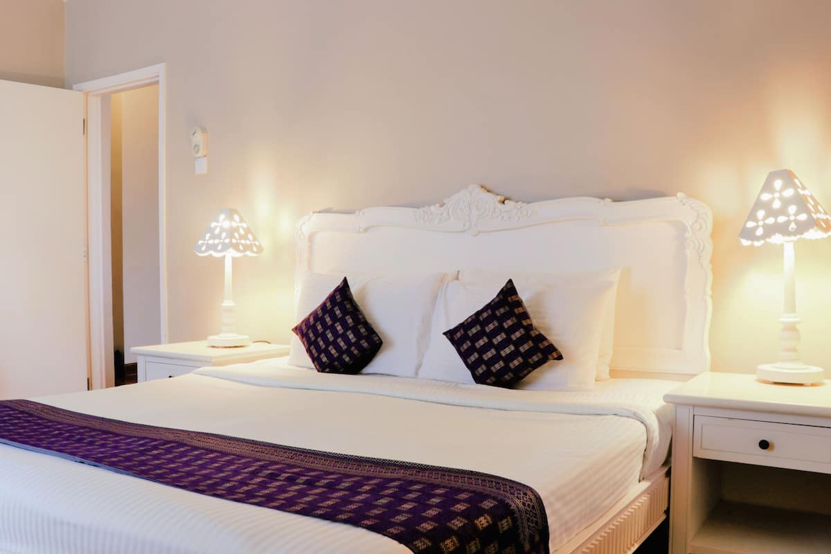 A neatly made bed with a patterned throw, two decorative pillows, and two bedside lamps on white nightstands.