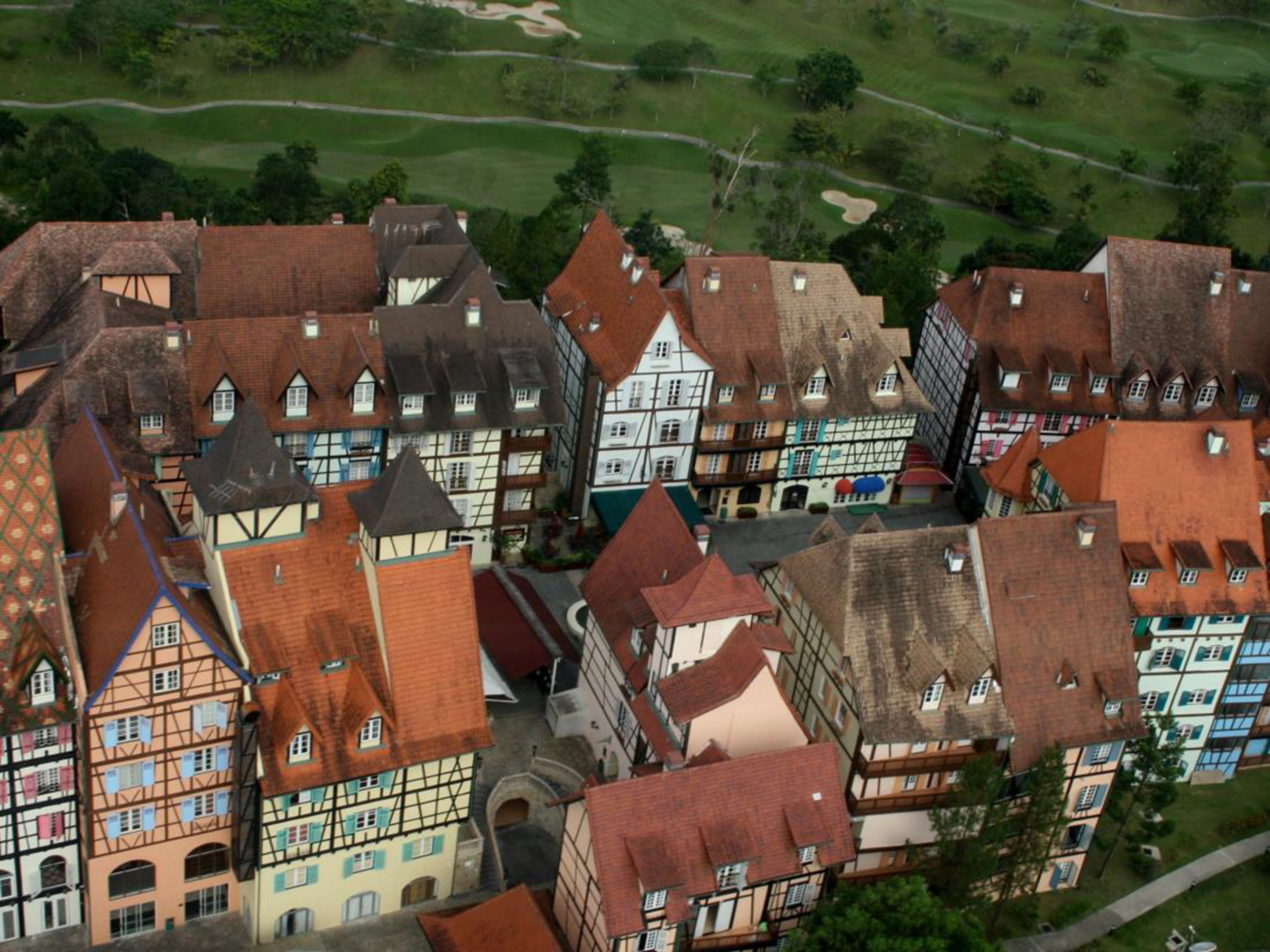 Un pueblo europeo tradicional con casas de entramado de madera, calles estrechas y un campo de golf al fondo.