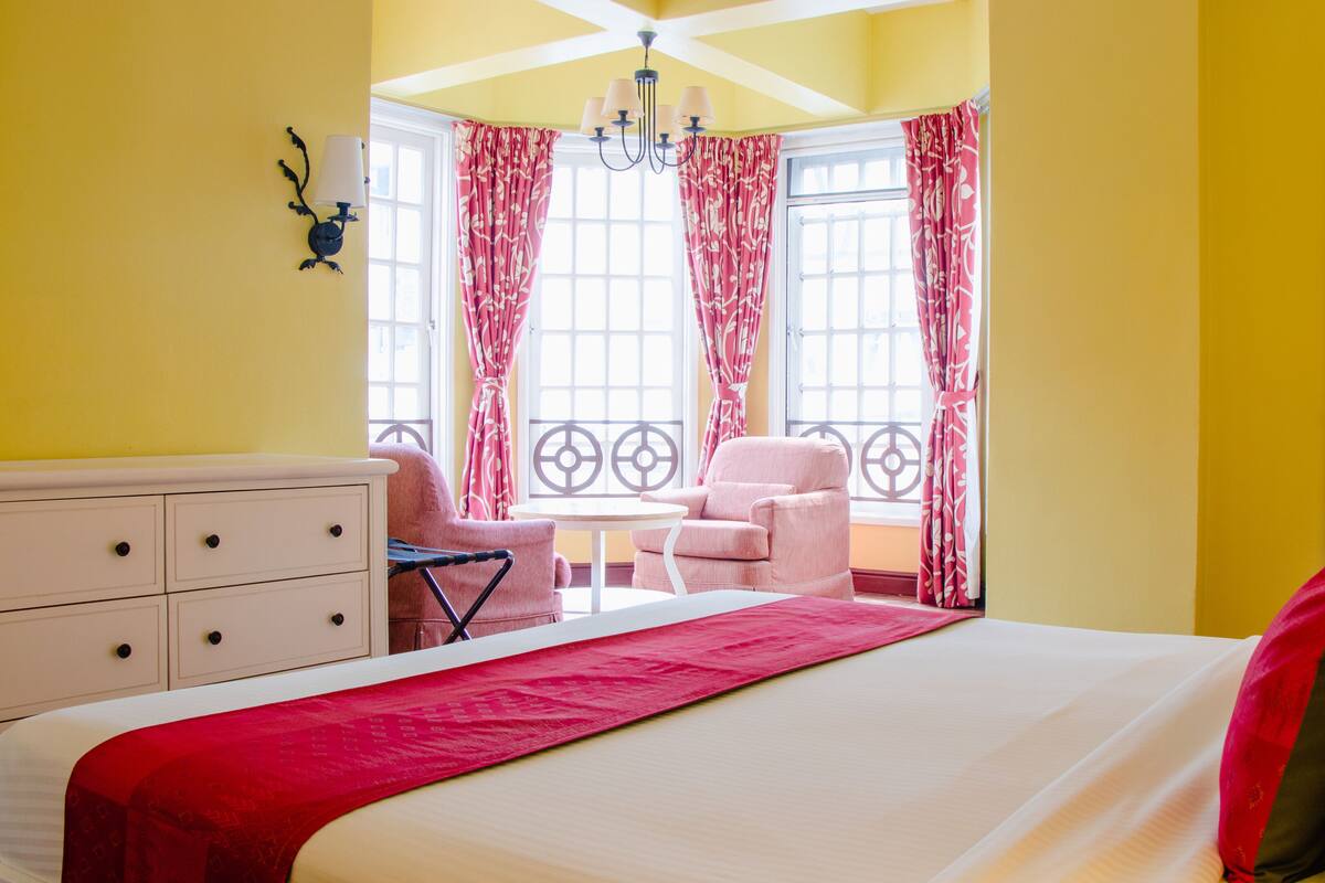 A hotel room with a bed, a desk, a chair, and a balcony with curtains.
