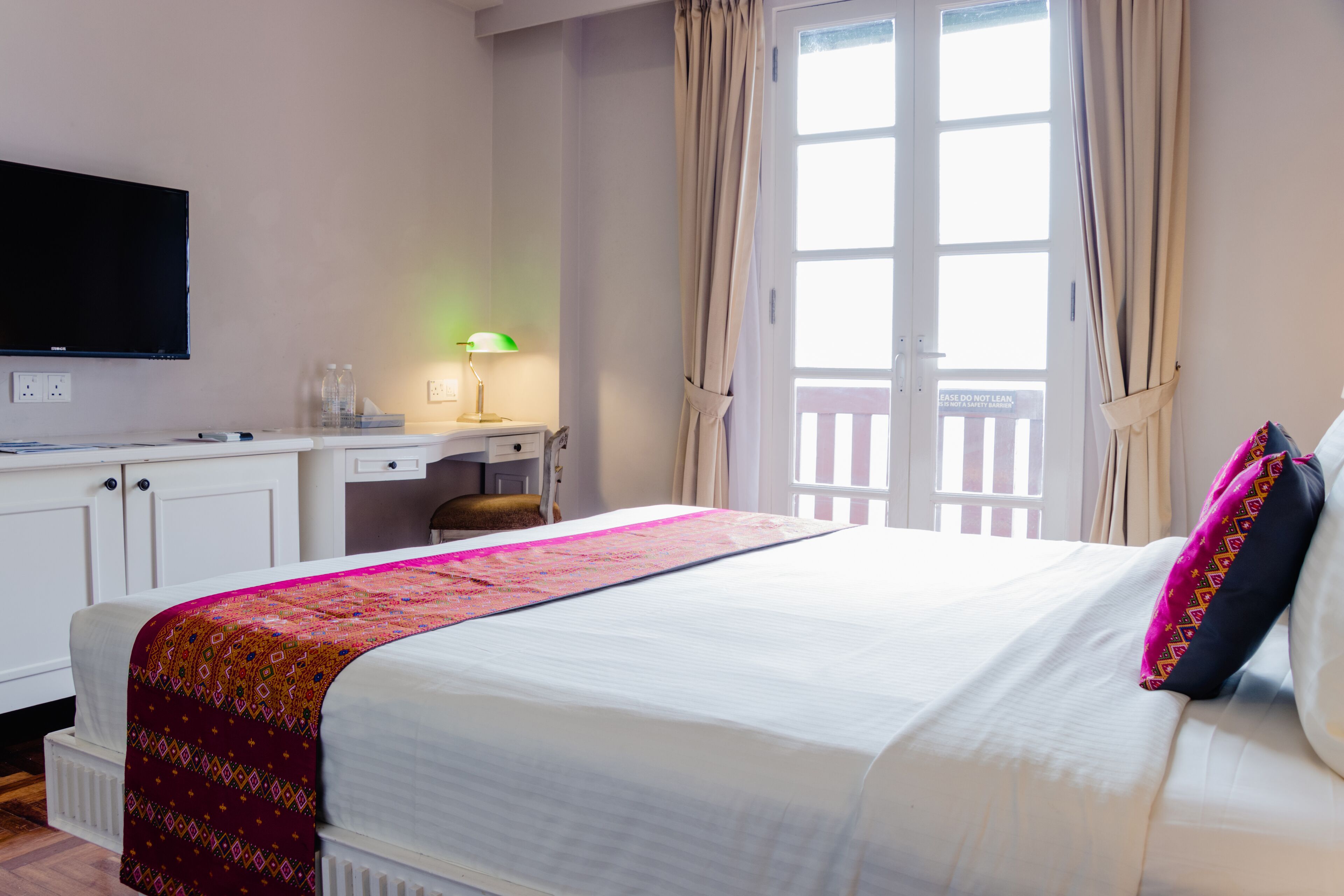 Una habitación de hotel con cama, escritorio, televisor y ventana con cortinas.
