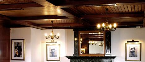 A dining area with a fireplace, wooden paneling, and a chandelier.