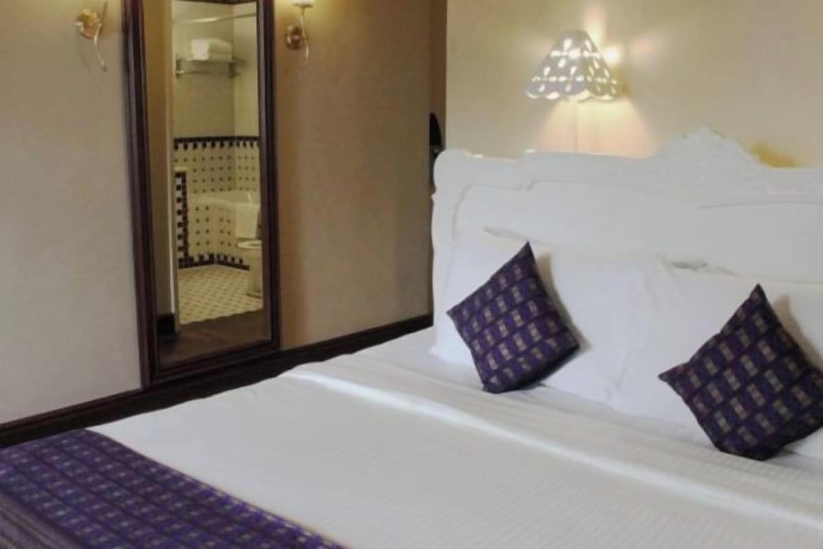 Une chambre d’hôtel avec un lit, un miroir et un luminaire fixé au mur.