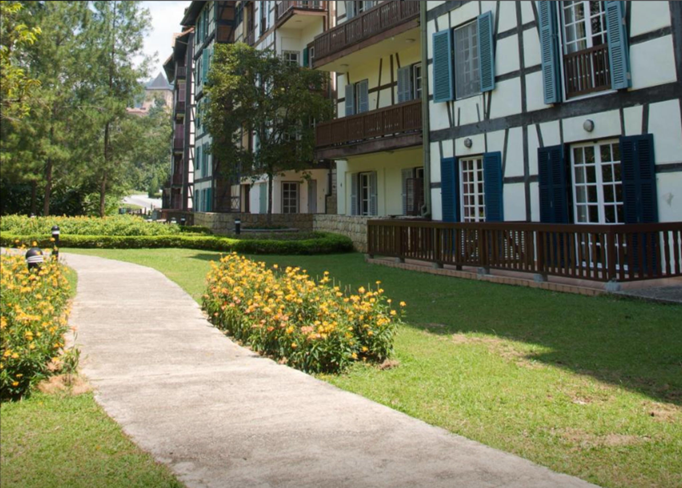 A traditional European-style building with a pathway leading to a well-maintained garden with yellow flowers.
