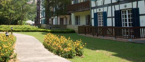A traditional European-style building with a pathway leading to a well-maintained garden with yellow flowers.