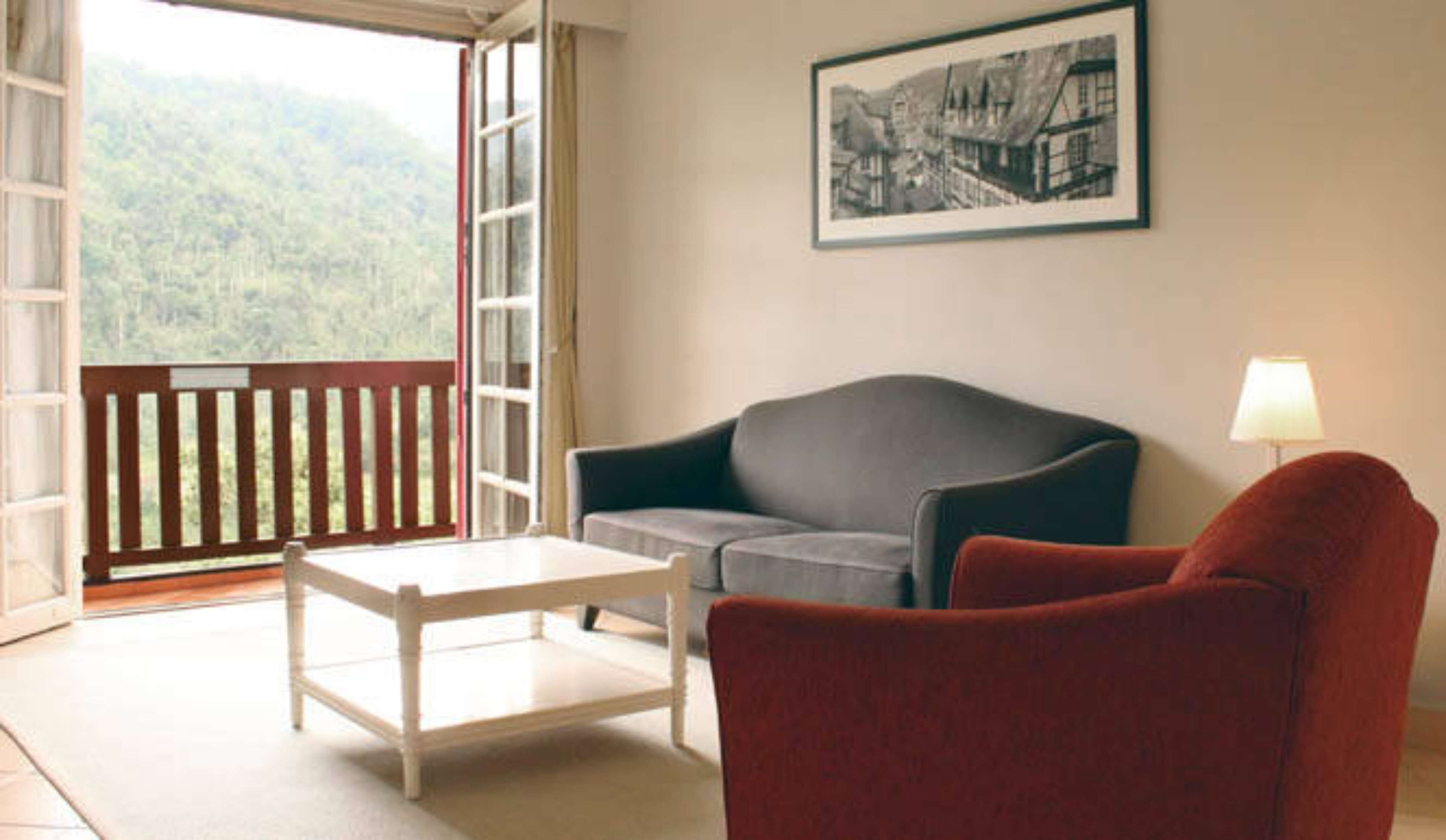 A room with a balcony, a grey sofa, a red armchair, and a small table.