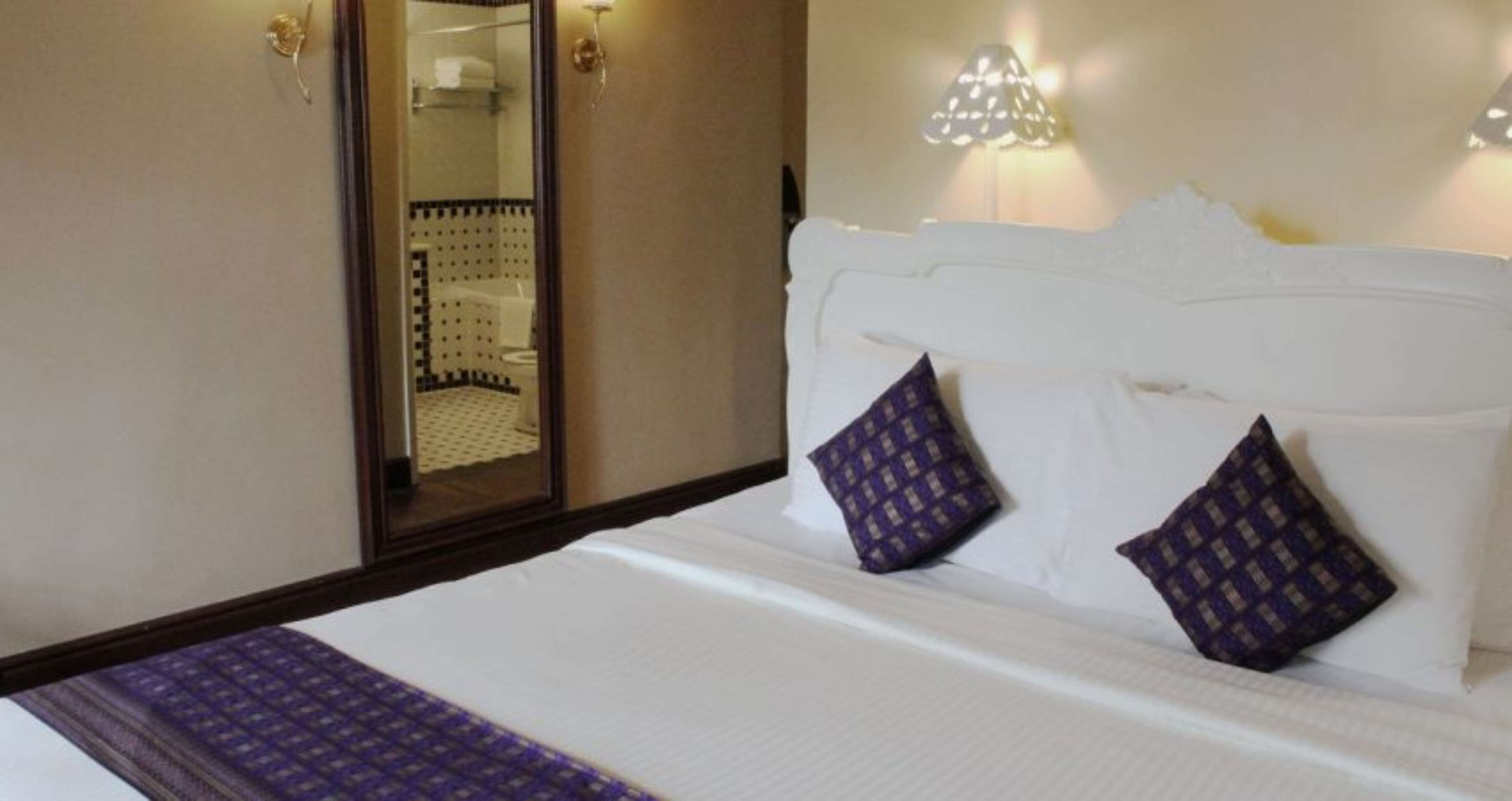 Ein Hotelzimmer mit einem Bett, zwei Kissen, einem Nachttisch und einem Spiegel.