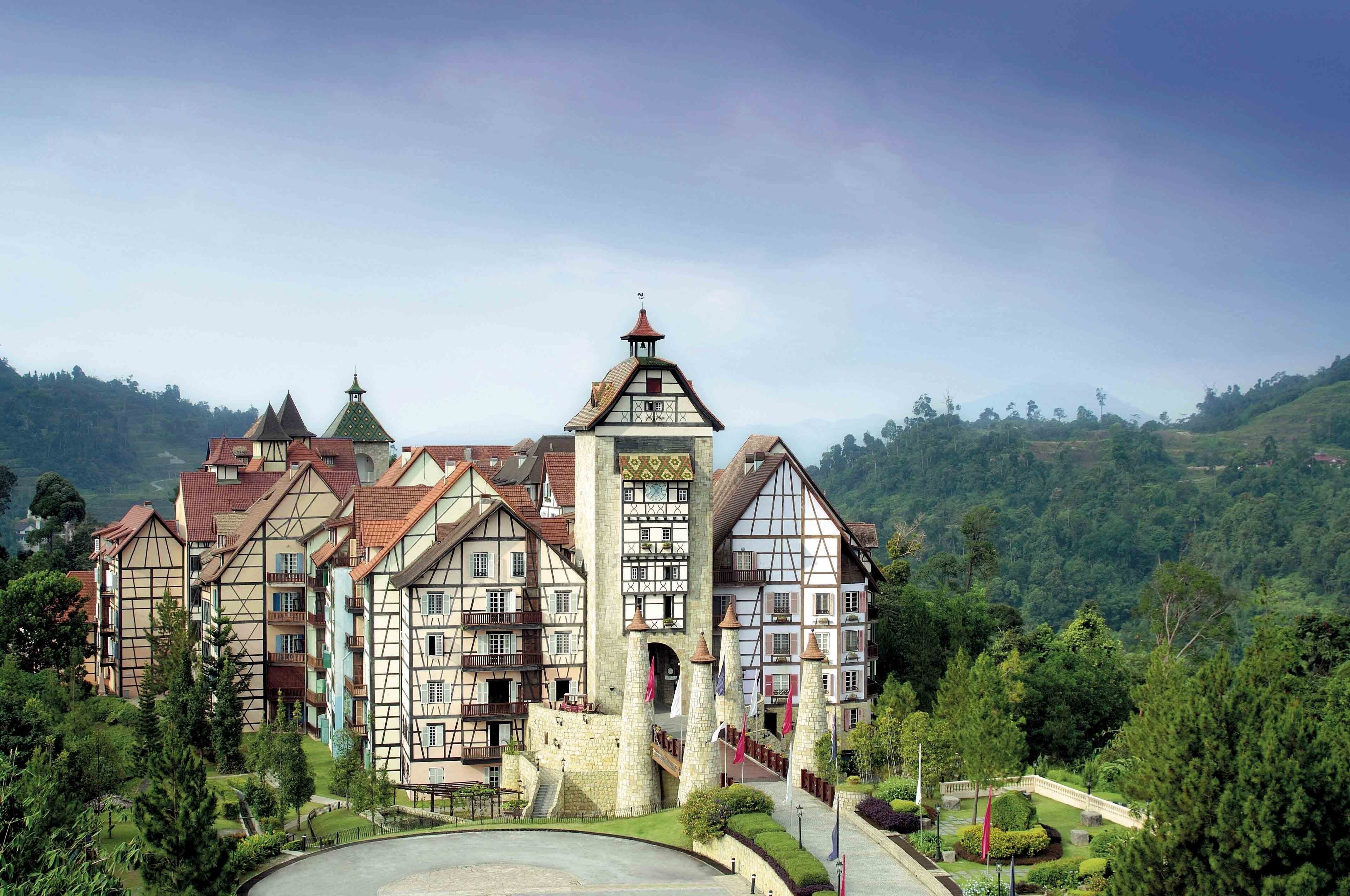 Un bâtiment traditionnel à colombages, comprenant plusieurs étages, une tour centrale et un jardin paysager qui l’entoure.