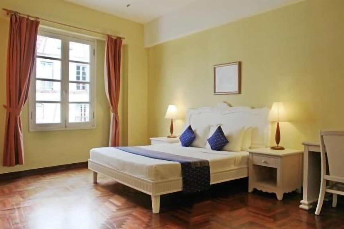 A hotel room with a bed, two bedside tables with lamps, a chair, and a window with curtains.