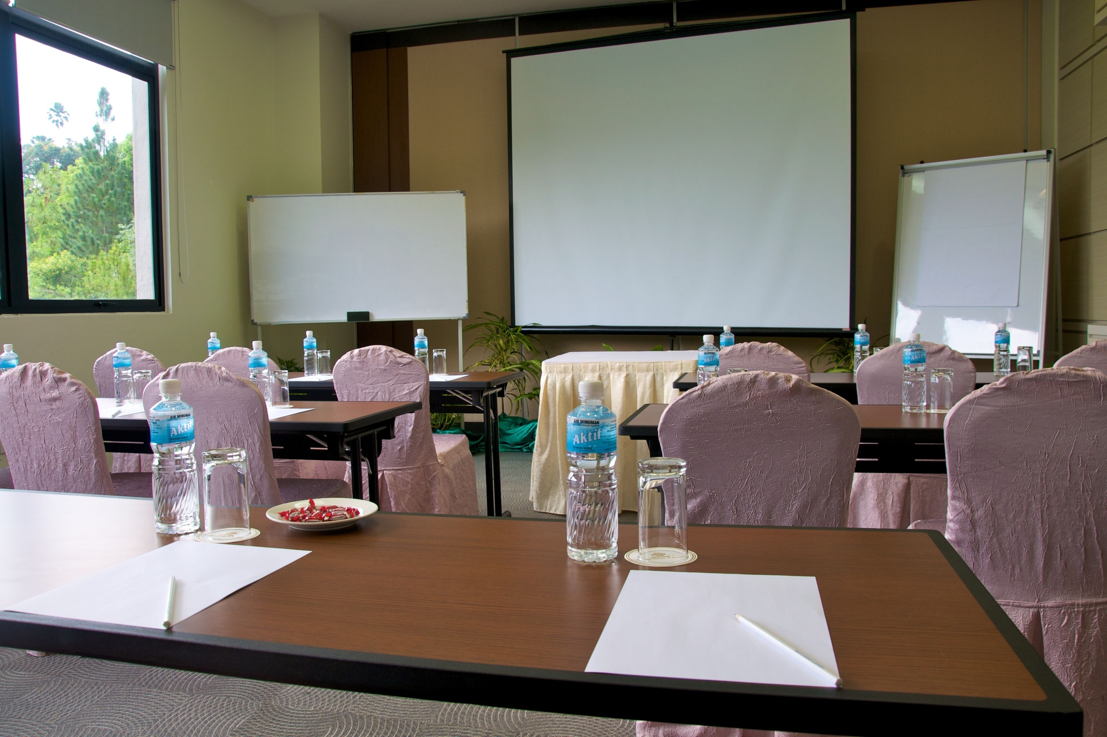 A conference room with tables, chairs, water bottles, and a projector screen.