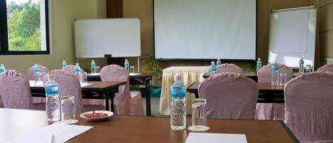 A conference room with tables, chairs, water bottles, and a projector screen.