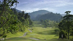 A golf course with a winding path, lush greenery, and a distant hill with a structure. - Colmar Tropicale (Bukit Tinggi)