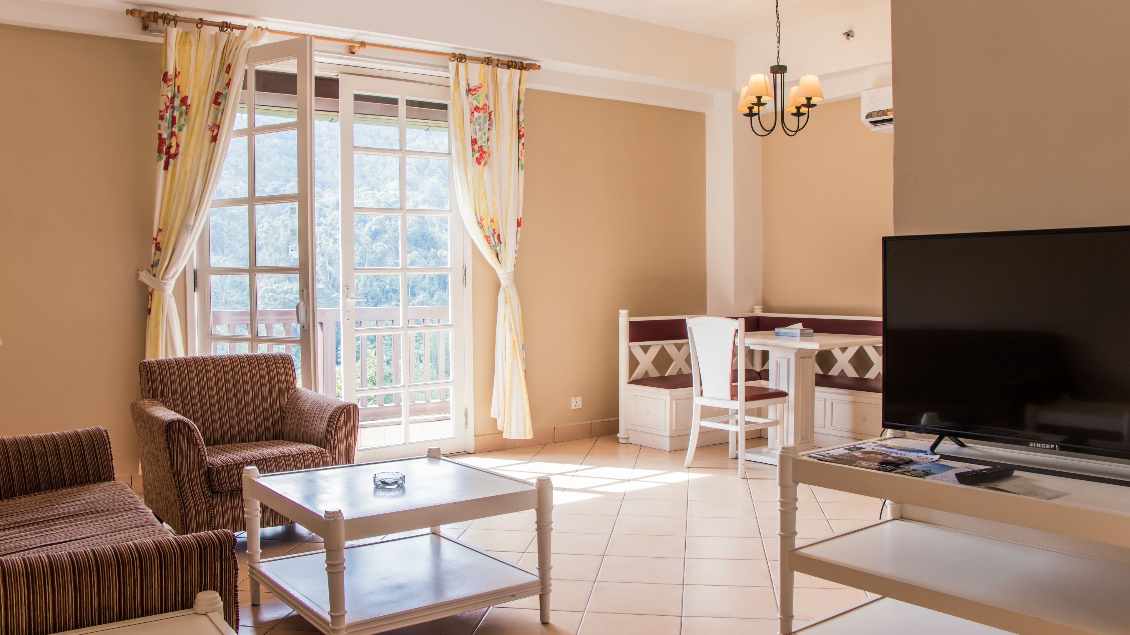 A living room with a sofa, a dining table, a TV, and a window with curtains.