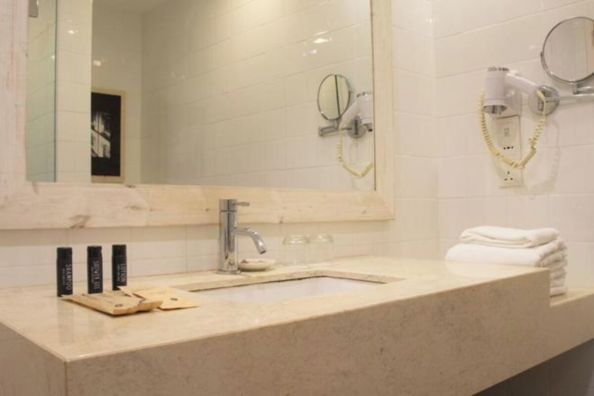 Un baño con lavamanos, espejo, secador de pelo y toallero.
